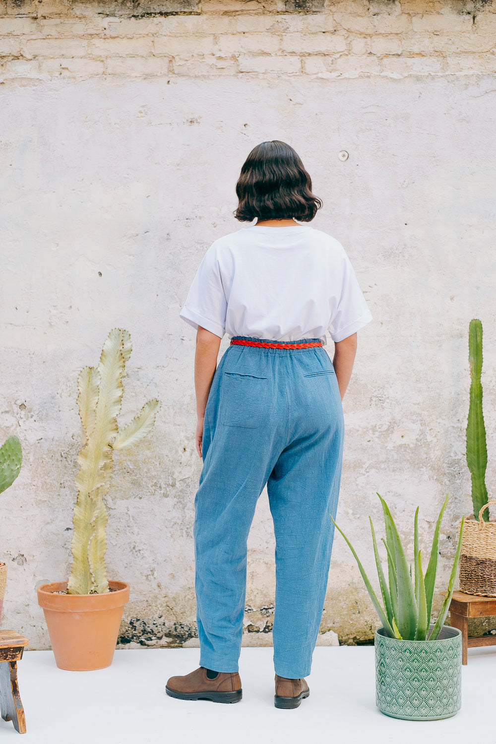 A person wearing a white crew neck t-shirt with a hand-crocheted red and yellow cactus and sun motif, paired with a blue skirt and a red belt.