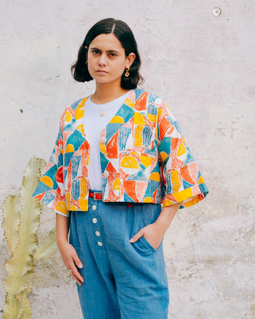 A colorful geometric patterned linen jacket with a V-neckline, elbow length sleeves, and a cropped fit.
