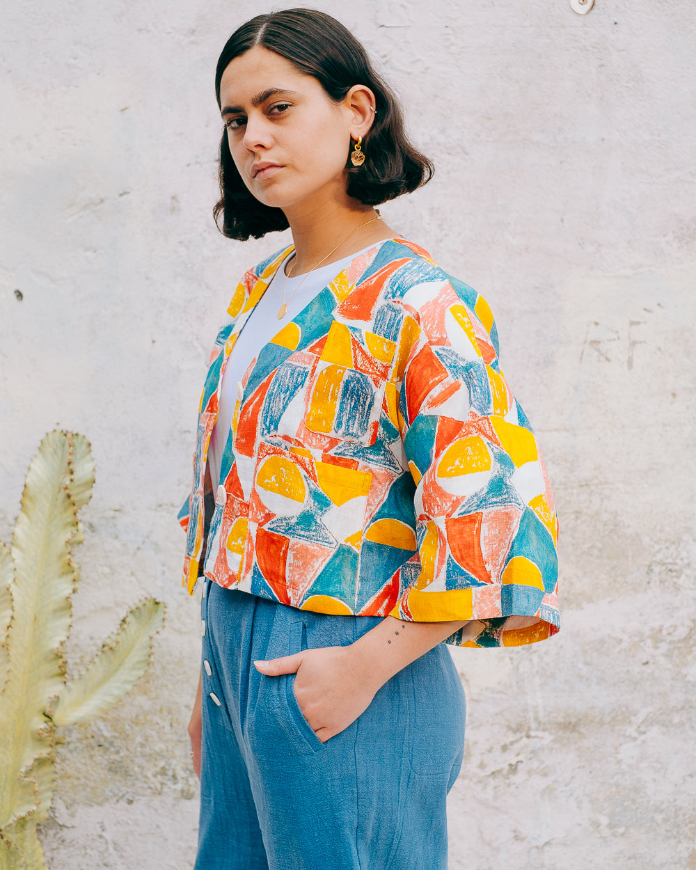 A colorful geometric patterned linen jacket with a V-neckline, elbow length sleeves, and a cropped fit.