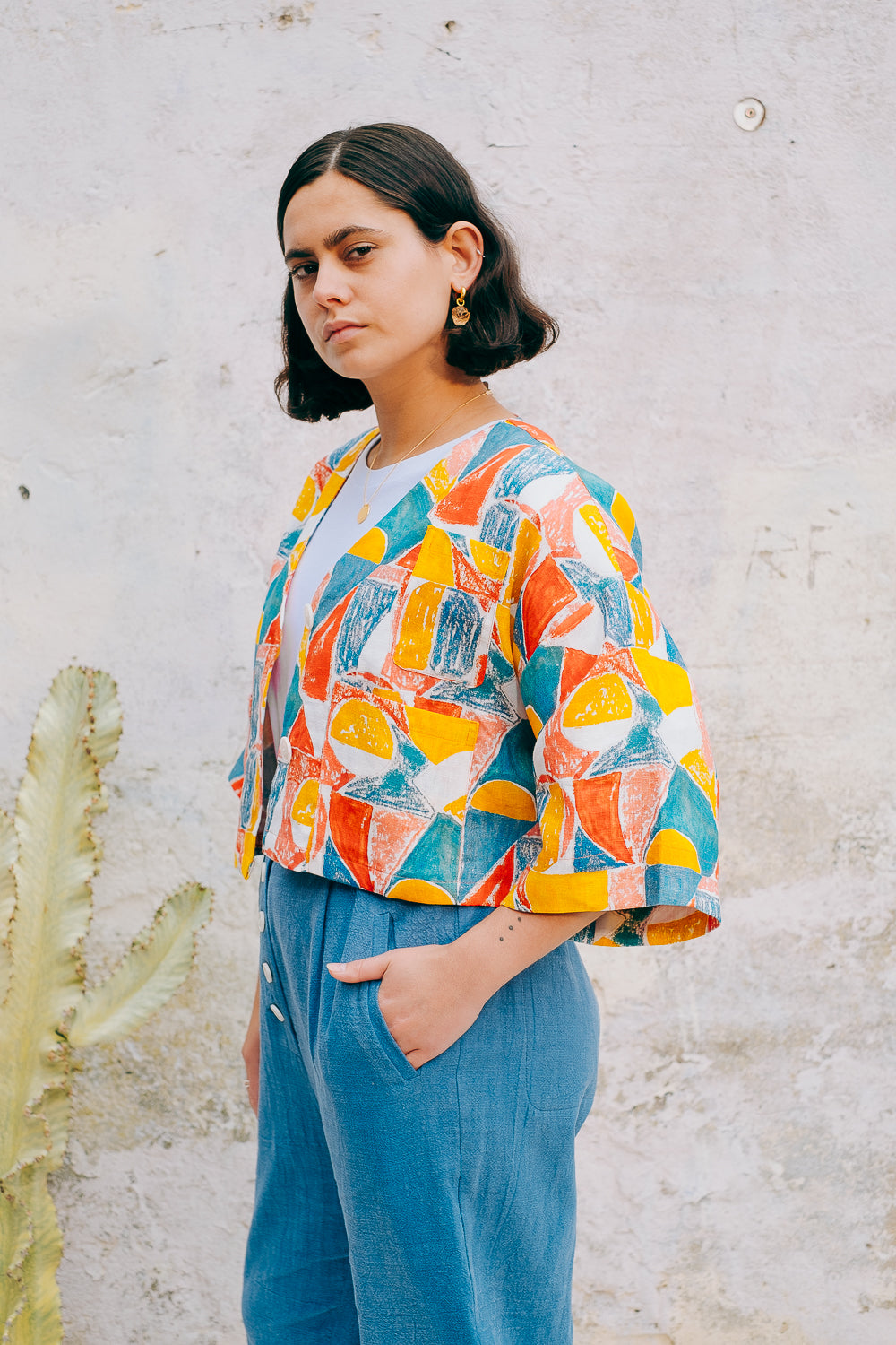 A colorful geometric patterned linen jacket with a V-neckline, elbow length sleeves, and a cropped fit.