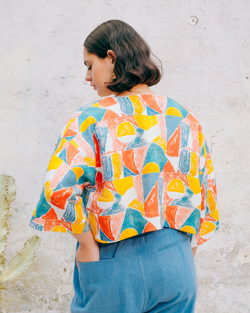 A colorful geometric patterned linen jacket with a V-neckline, elbow length sleeves, and a cropped fit.