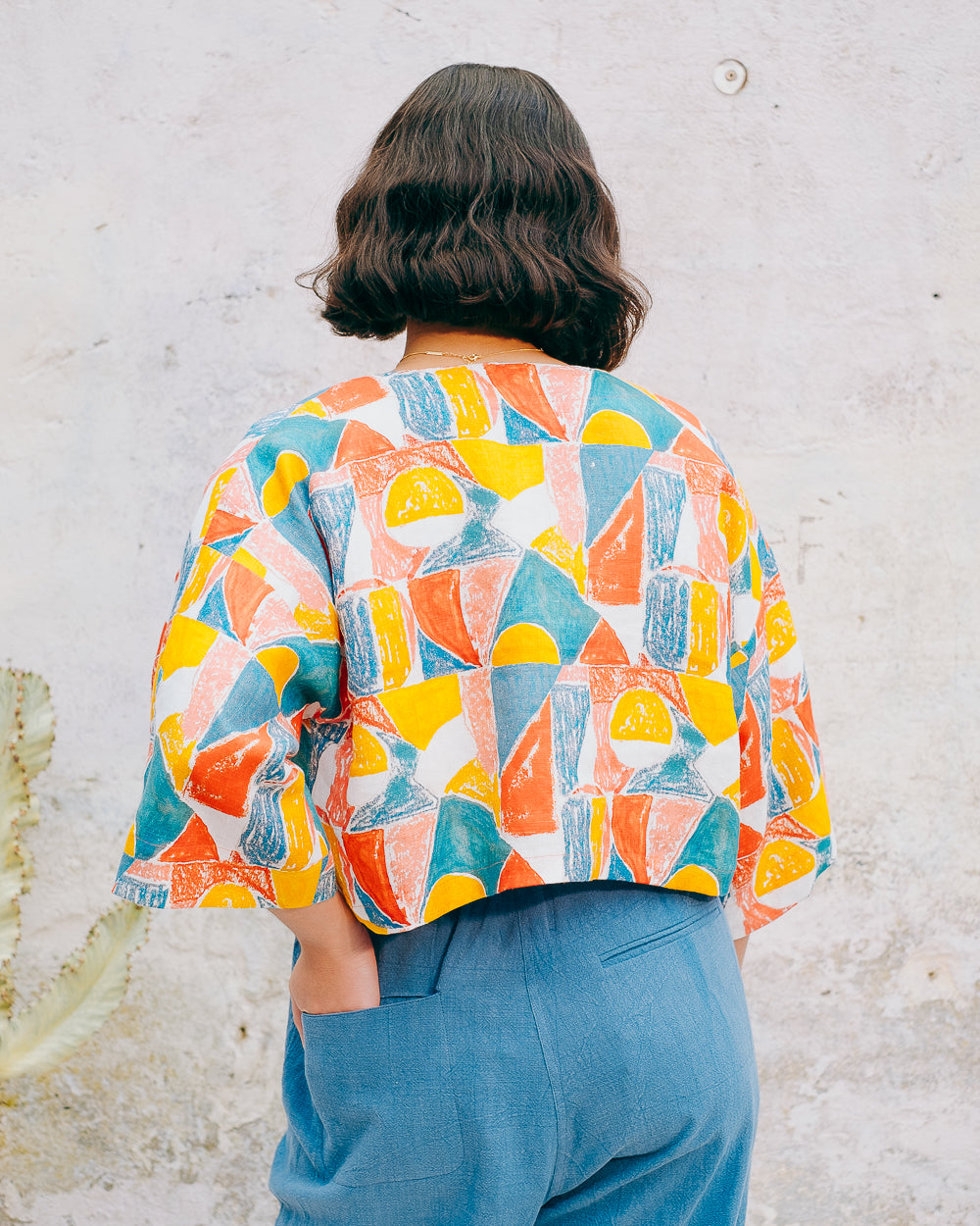 A colorful geometric patterned linen jacket with a V-neckline, elbow length sleeves, and a cropped fit.