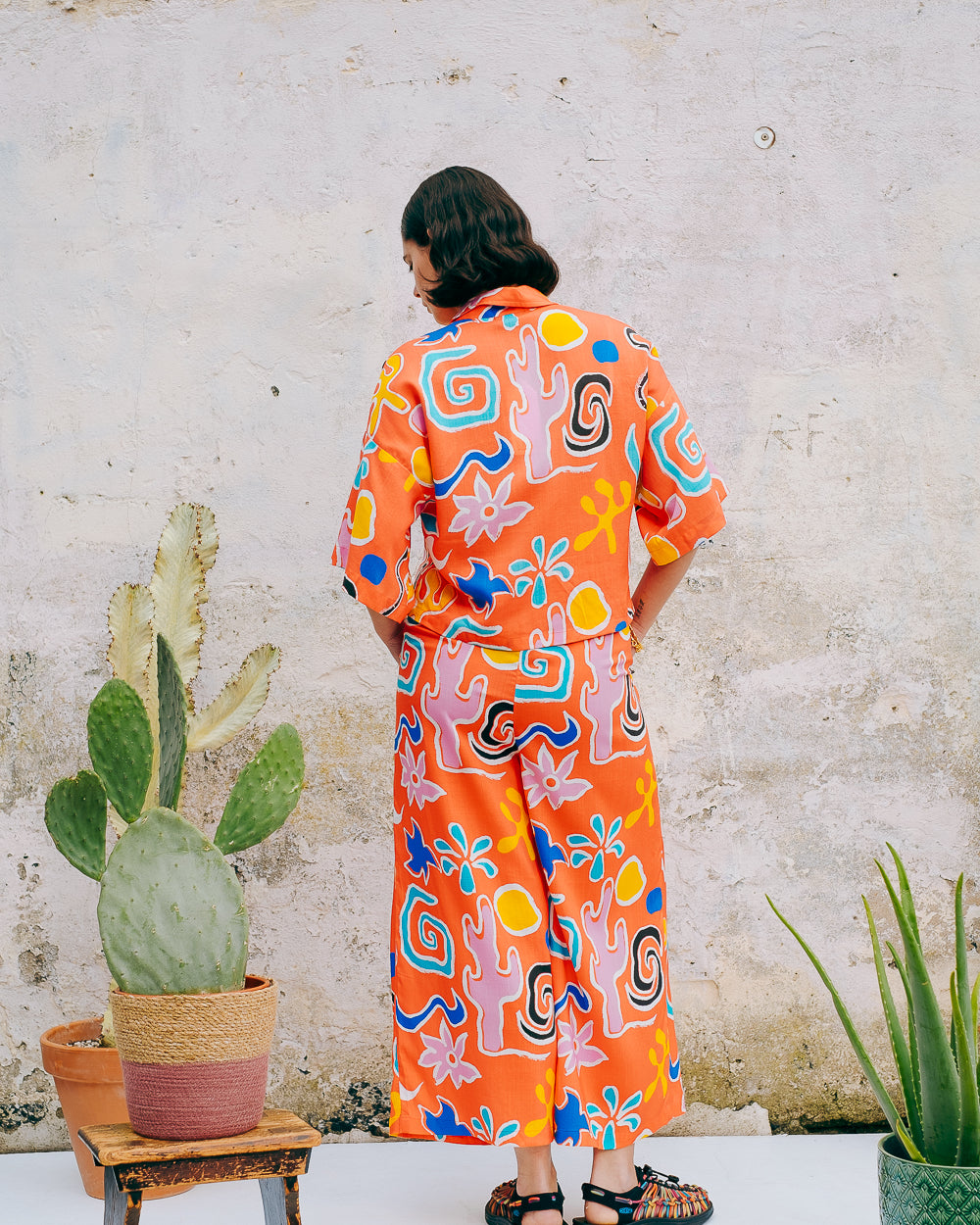 A pair of wide leg cropped trousers with a desert print in vibrant bright orange, featuring front pleats, an elasticated back waist, button and zip on the side, and side pockets.