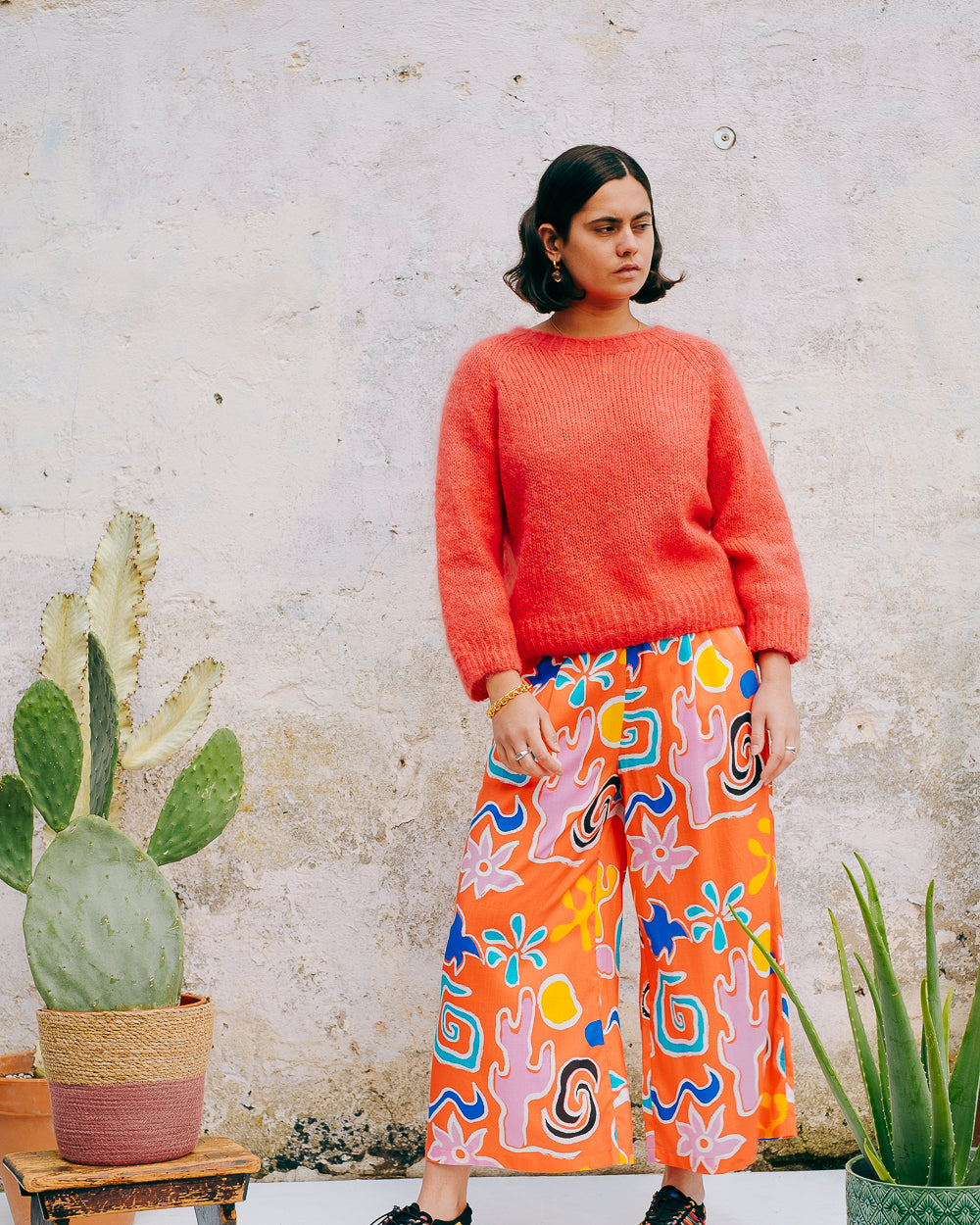 A pair of wide leg cropped trousers with a desert print in vibrant bright orange, featuring front pleats, an elasticated back waist, button and zip on the side, and side pockets.