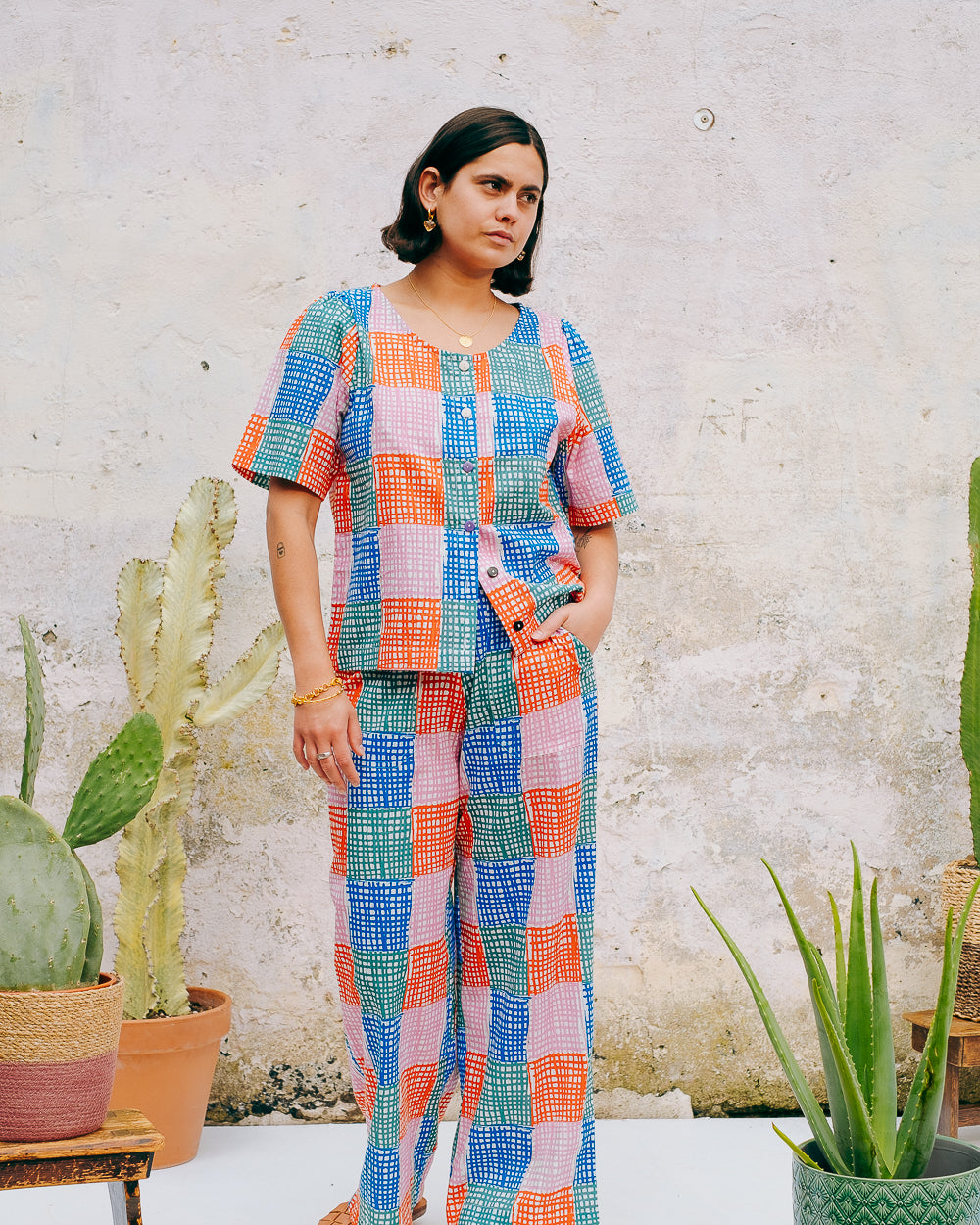 A pair of straight leg trousers with a multicolored grid check pattern. The trousers have a flat front, elasticated waist at the back, and side patch pockets.