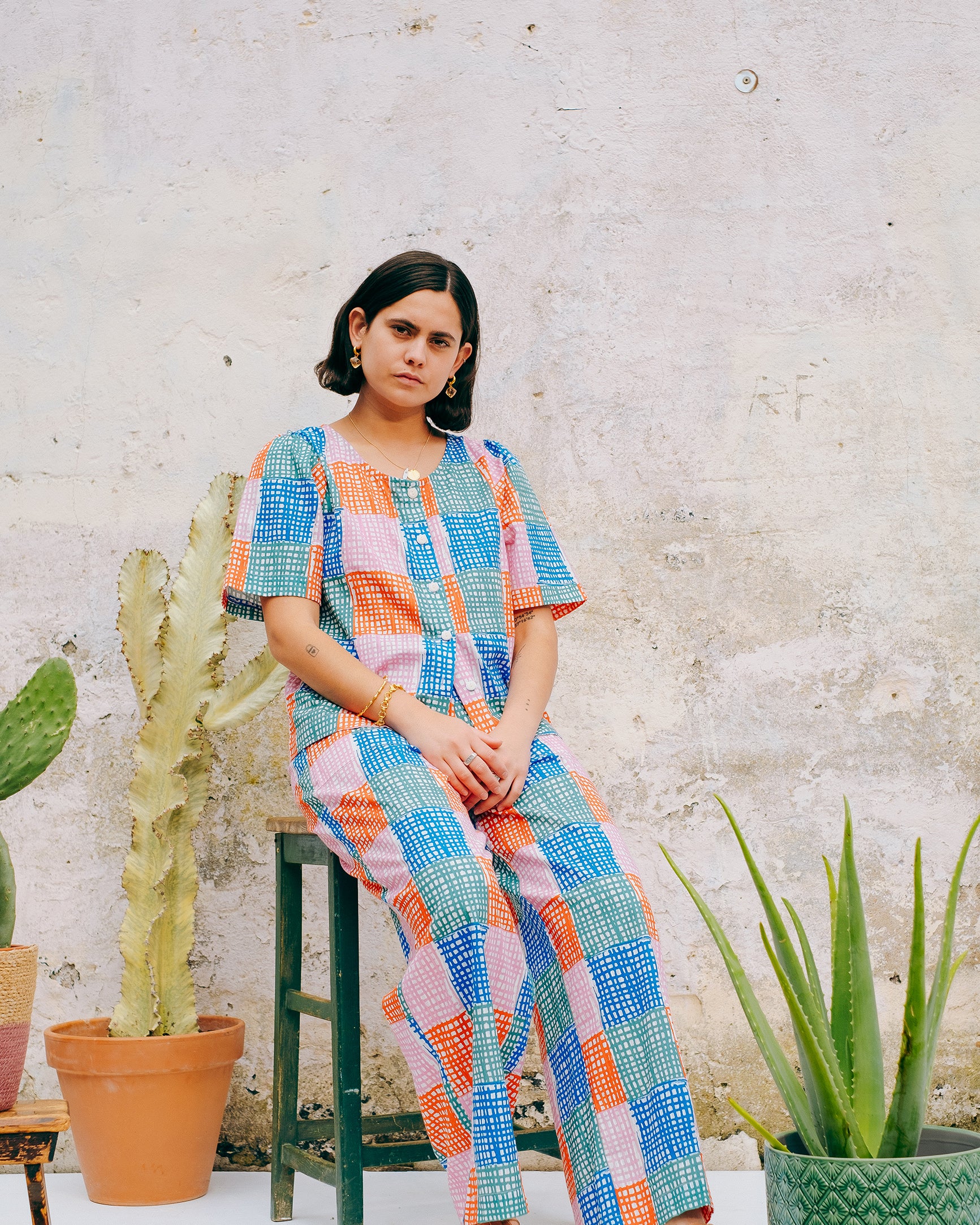 A pair of straight leg trousers with a multicolored grid check pattern. The trousers have a flat front, elasticated waist at the back, and side patch pockets.