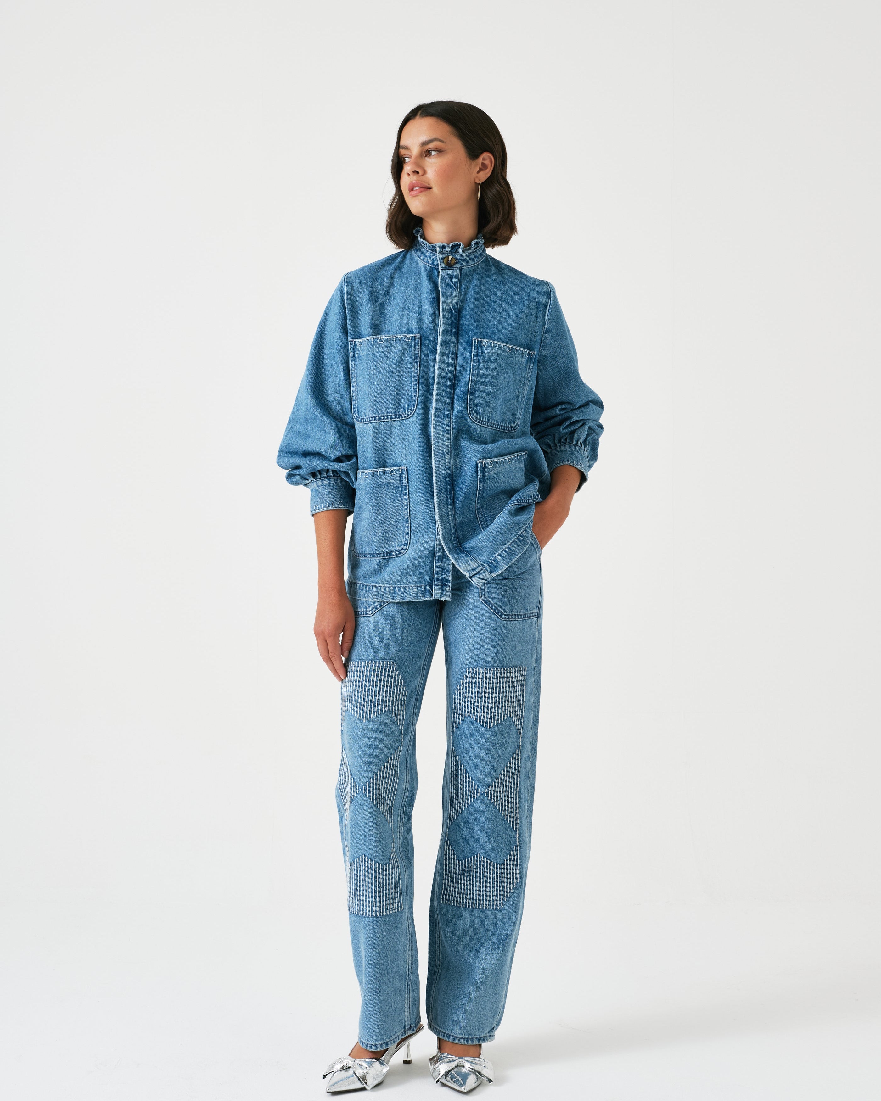 A pair of blue carpenter style jeans with embroidery on the front legs and a center front seam, displayed against a white background.