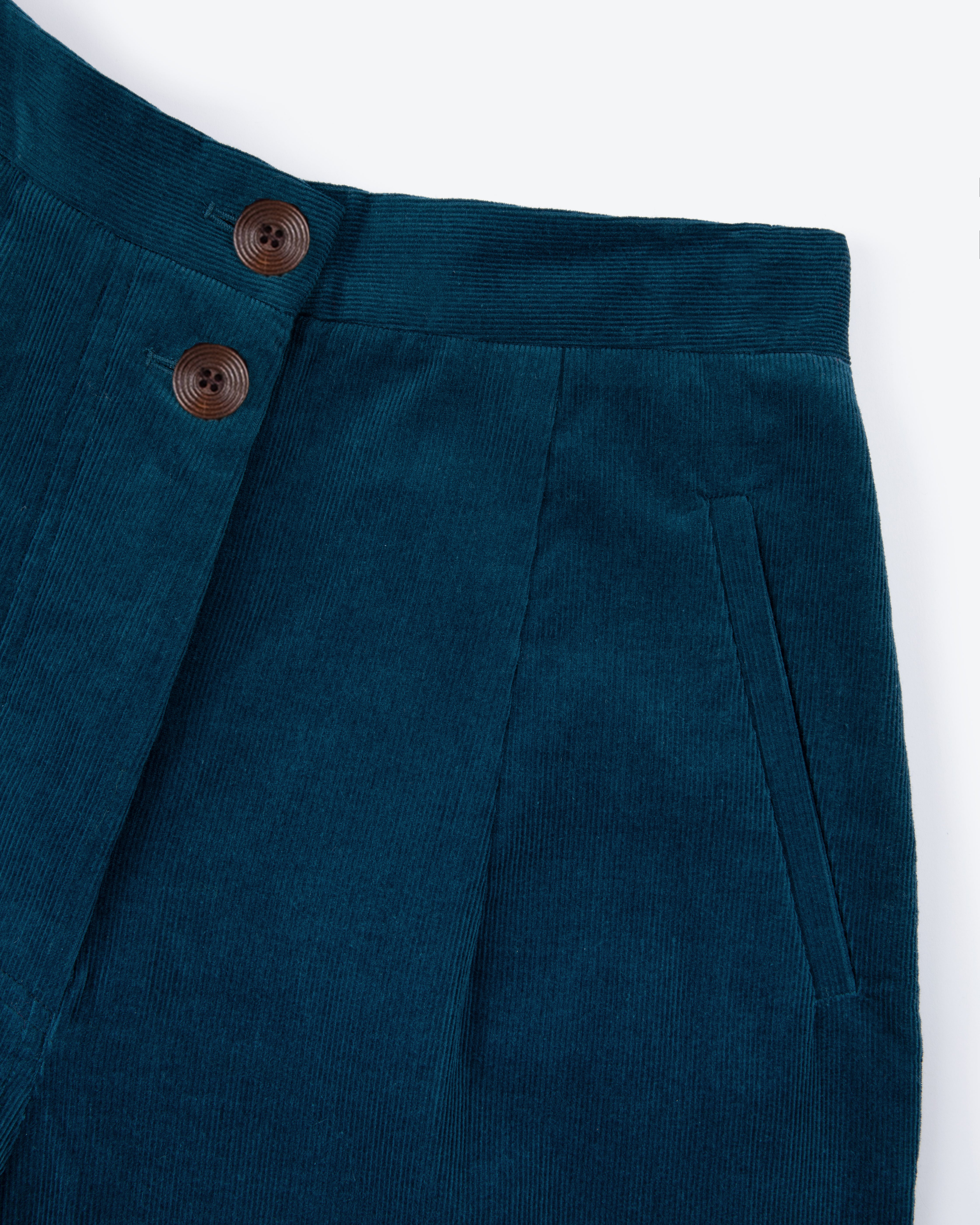 Close-up of teal pants with wooden buttons on a white background