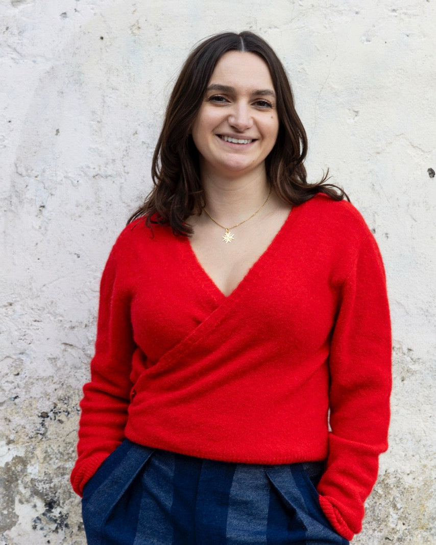 Woman wearing a red sweater and blue plaid pants against a textured white wall.