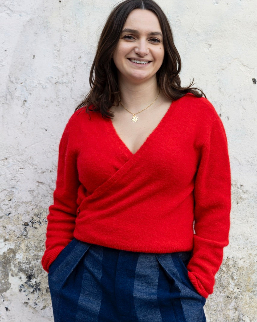 Woman wearing a red sweater and blue plaid pants against a textured white wall.