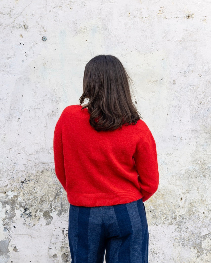 Person wearing a red sweater and blue pants standing against a textured white wall.