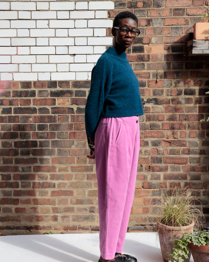 Person wearing a teal sweater and pink pants standing against a brick wall.