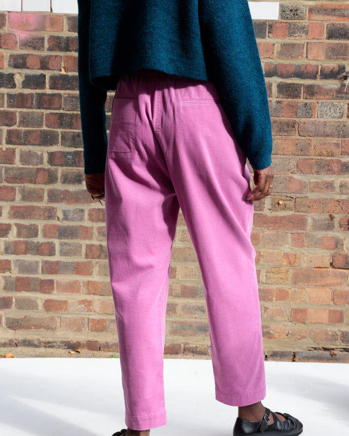 Person wearing pink pants and a blue sweater standing against a brick wall.