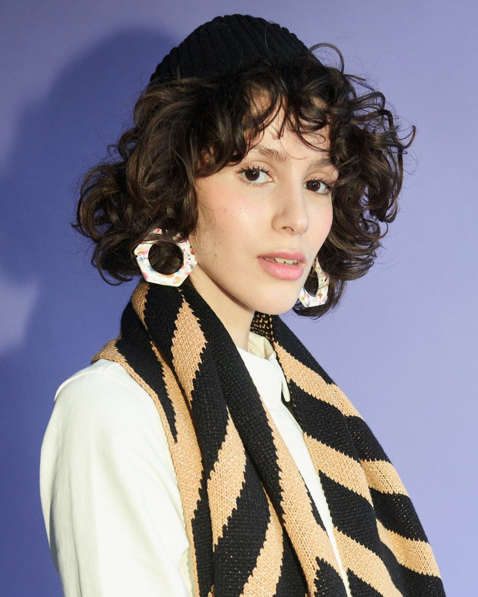 Person wearing a black and beige patterned scarf against a blue background.