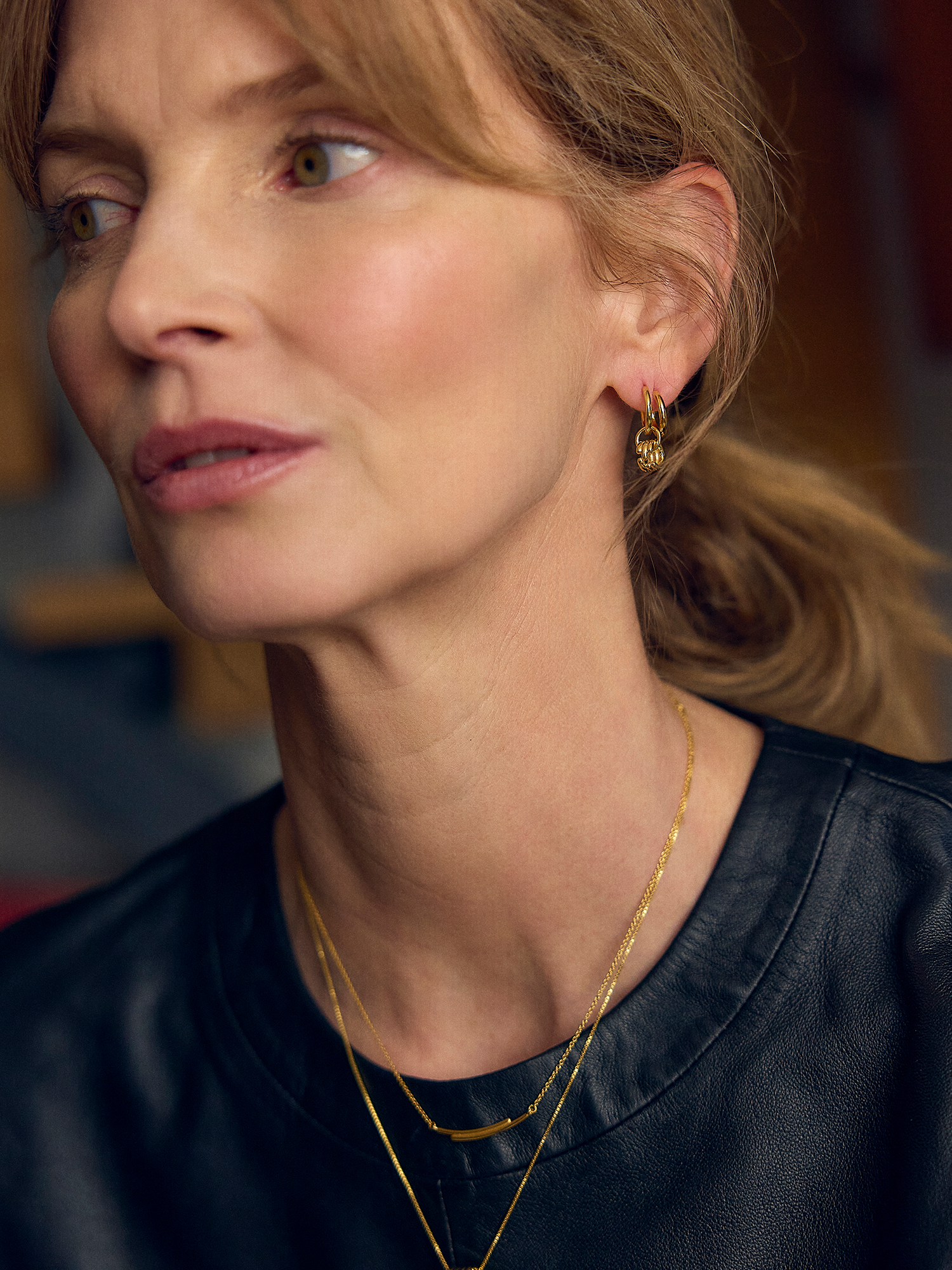 Close-up of a woman wearing gold earrings and necklaces with a blurred background