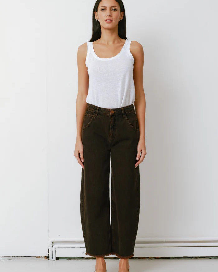 Woman wearing a white tank top and dark pants against a white background