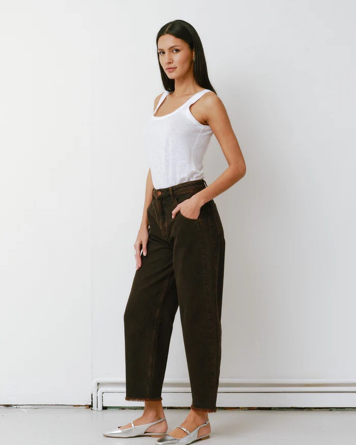 Woman wearing a white tank top and dark pants against a white wall