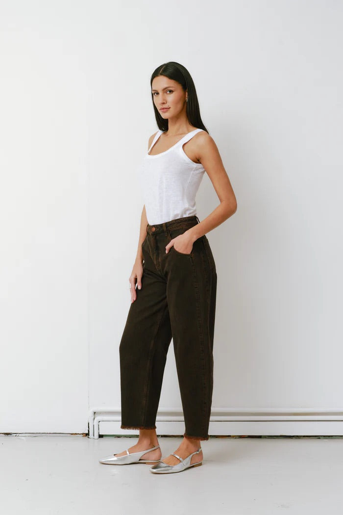 Woman wearing a white tank top and dark pants against a white wall