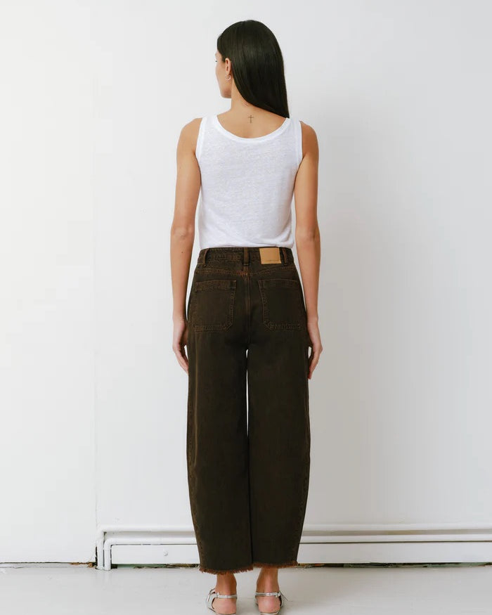 Person wearing a white tank top and dark green wide-leg pants against a white wall.