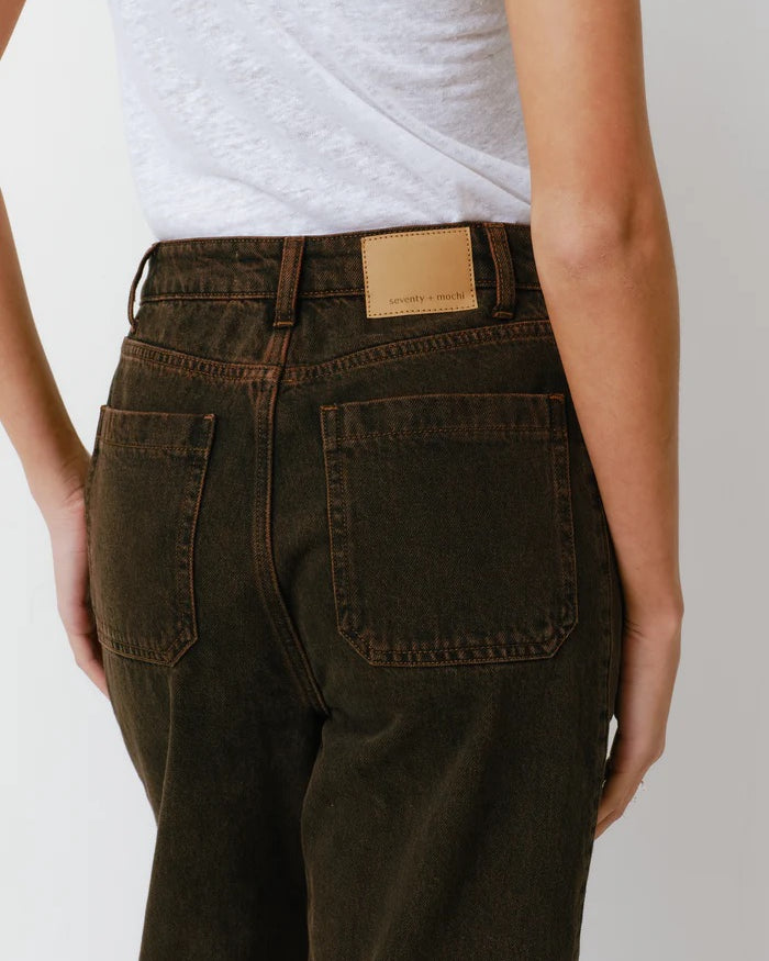 Person wearing dark brown pants with a visible brand label on a plain background