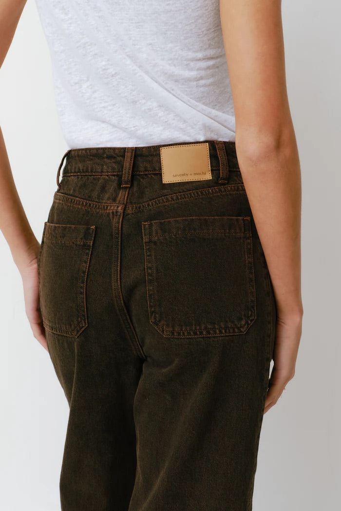 Person wearing dark brown pants with a visible brand label on a plain background