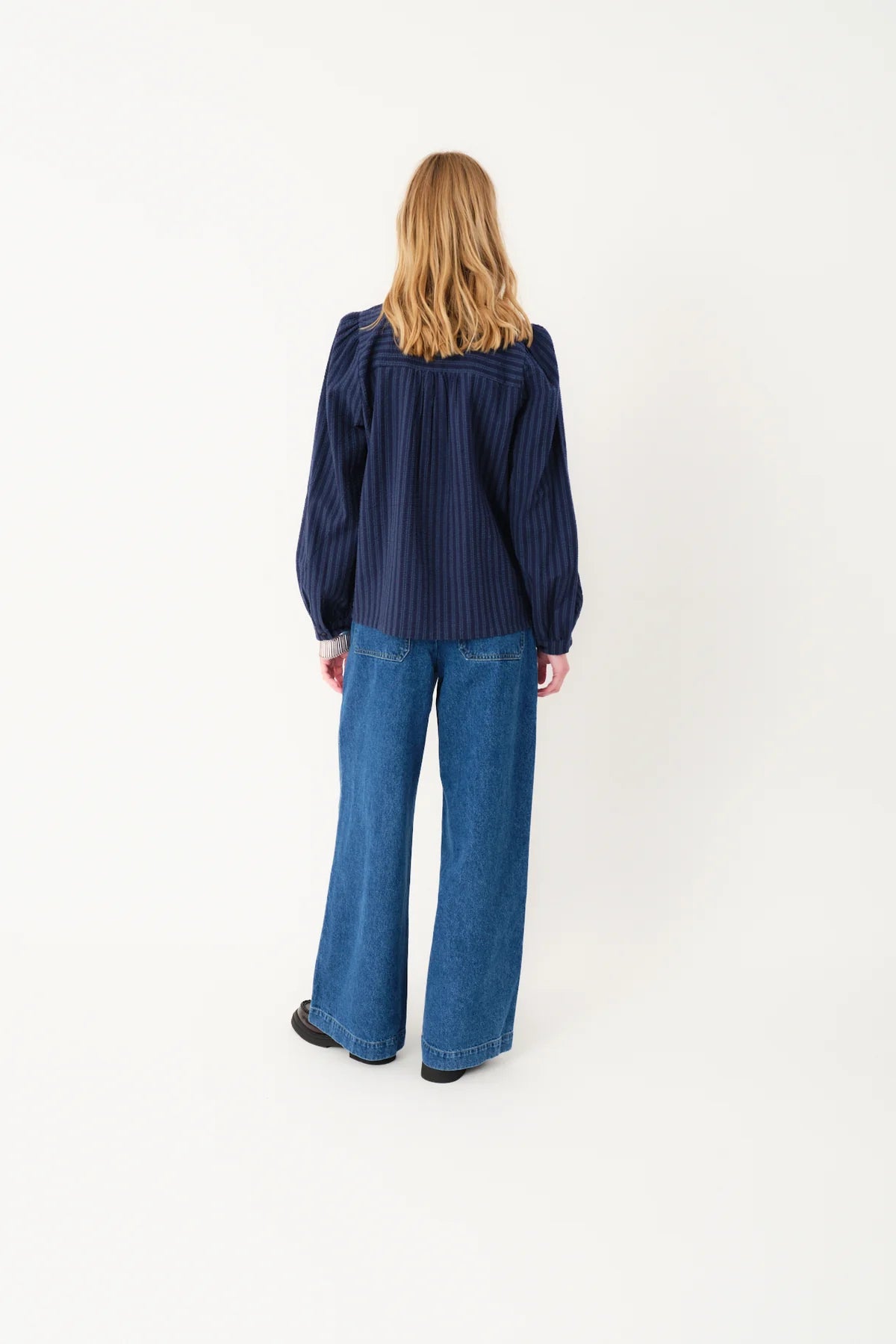 Person wearing a blue striped shirt and blue jeans on a white background