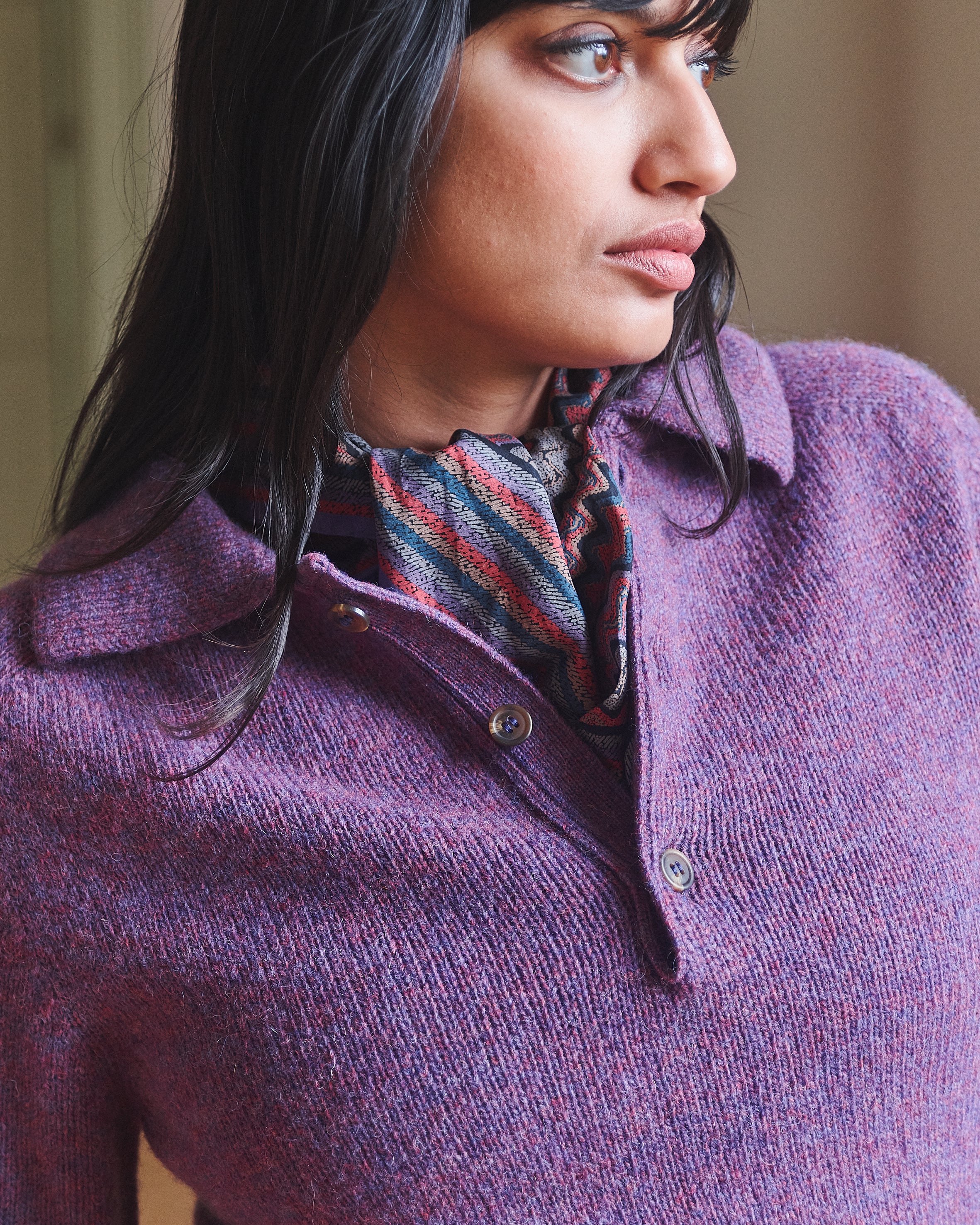 Woman wearing a purple sweater with a patterned scarf, looking to the side.