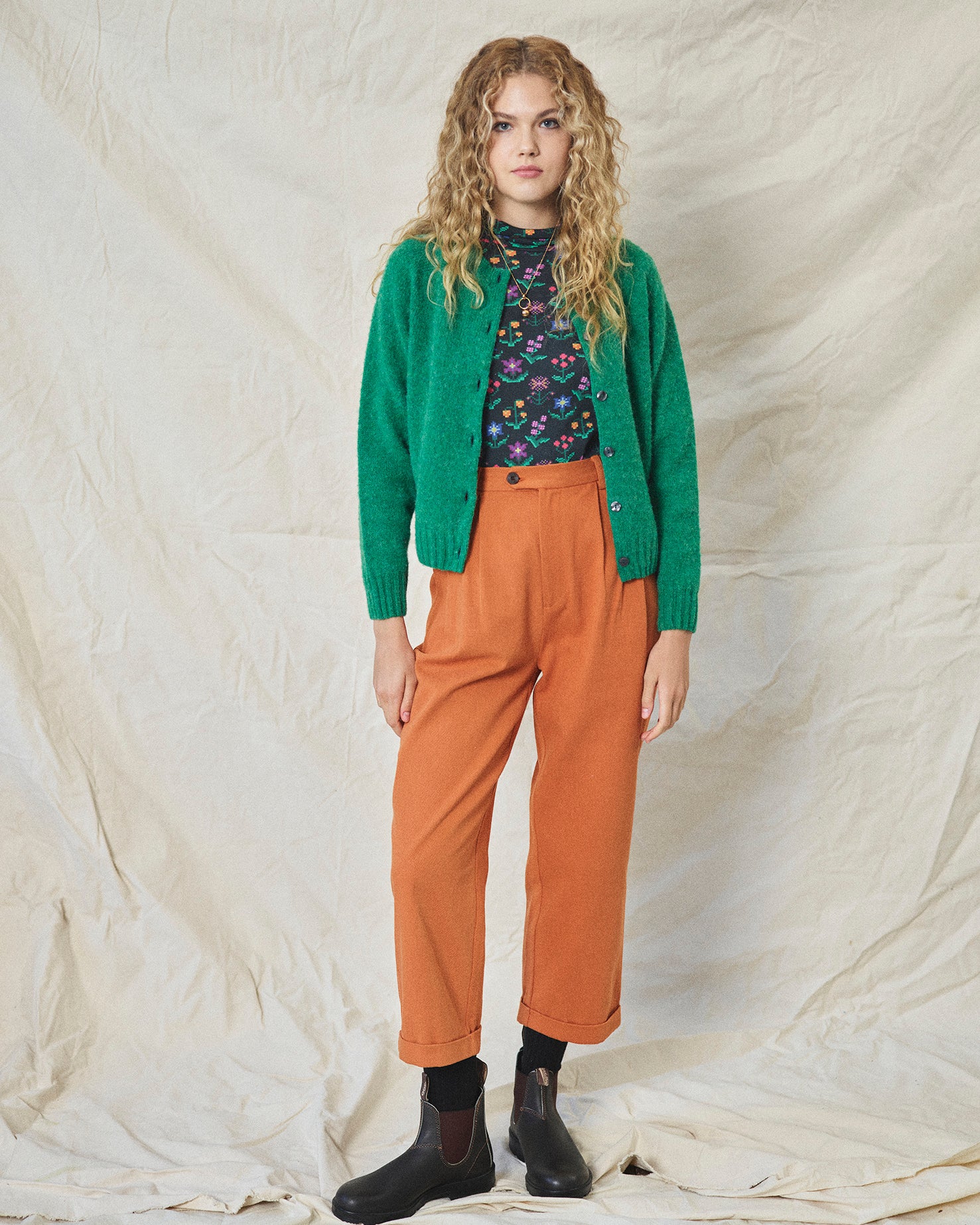 A pair of orange wide leg trousers with pleats and a fixed turn-up hem, made from cotton drill fabric.