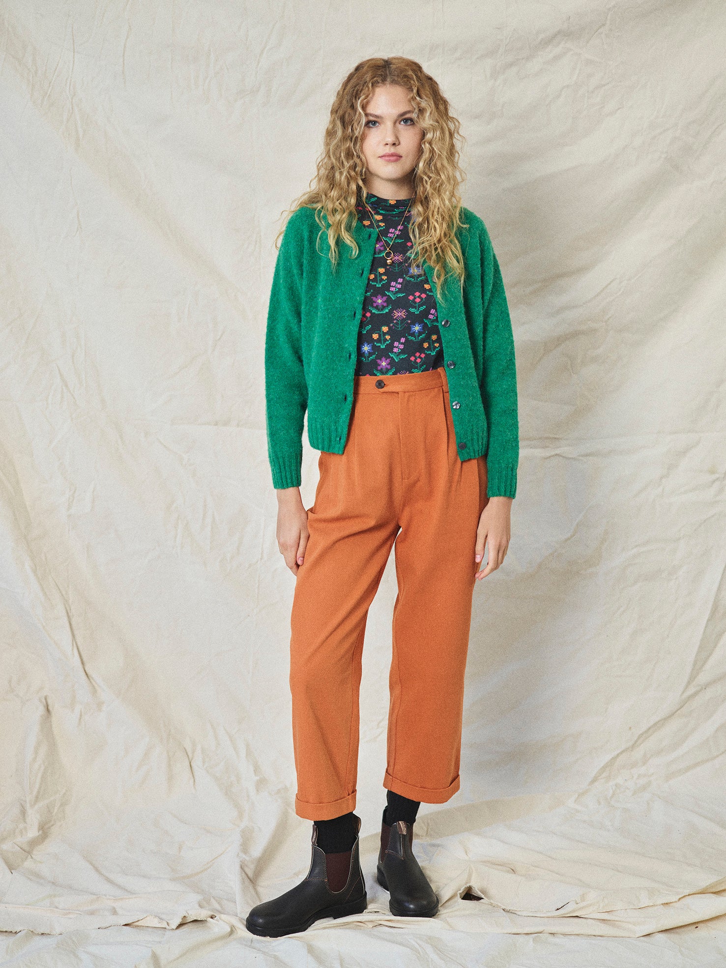 A pair of orange wide leg trousers with pleats and a fixed turn-up hem, made from cotton drill fabric.