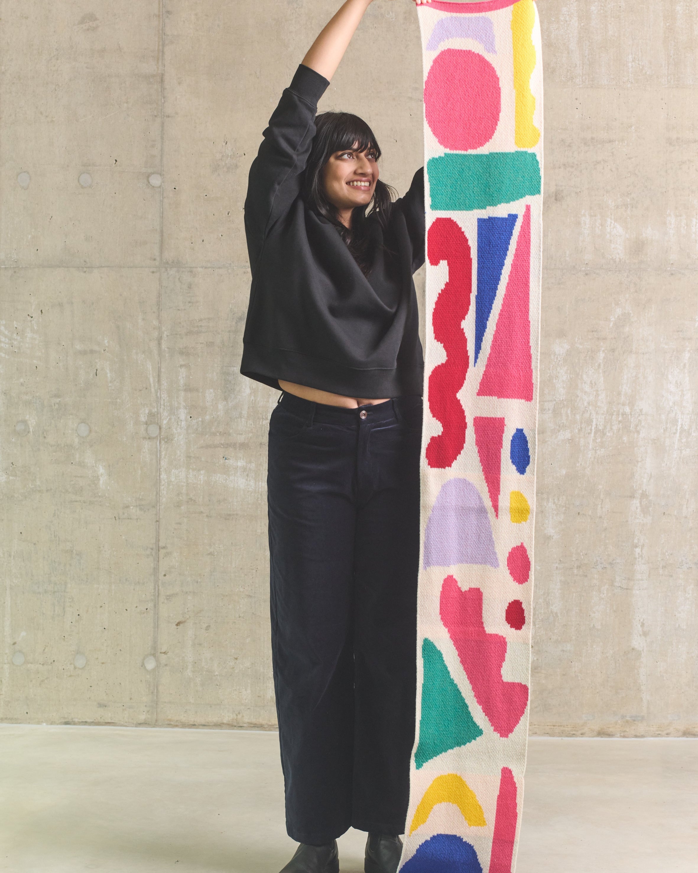 Person holding a colorful patterned scarf against a concrete wall.
