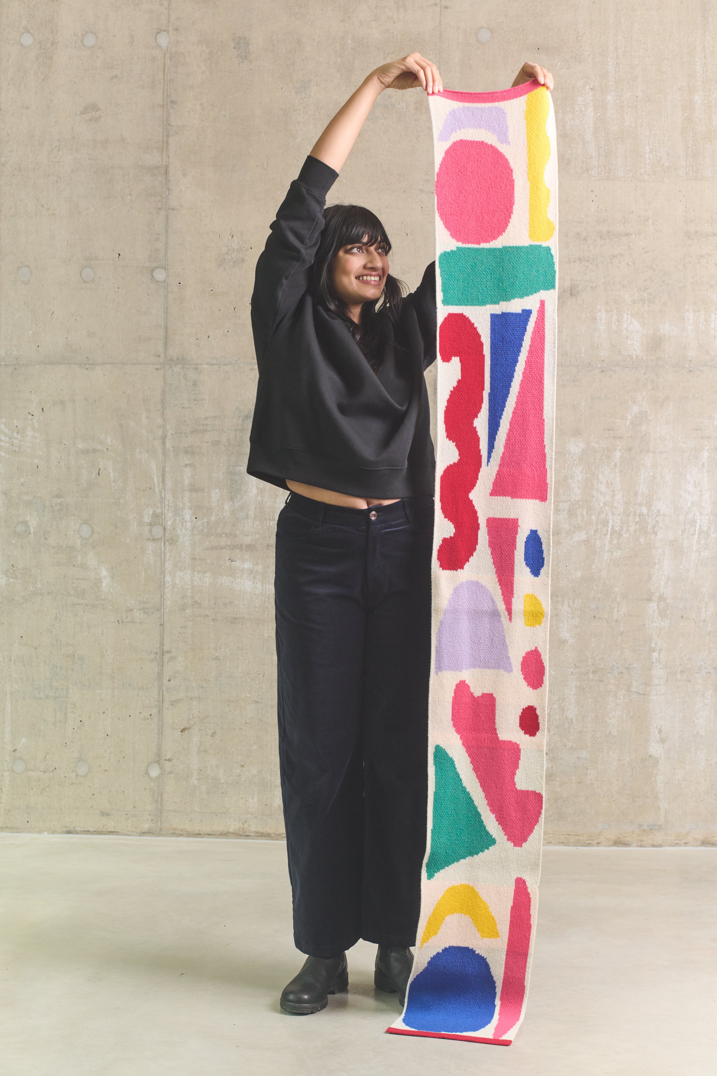 Person holding a colorful patterned scarf against a concrete wall.