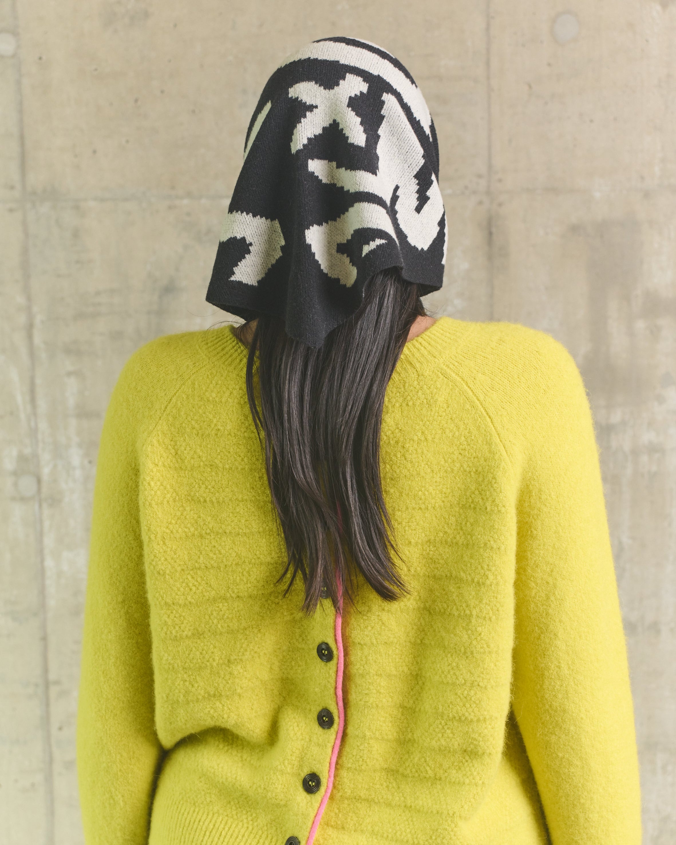 Person wearing a yellow cardigan and black and white patterned hat against a plain background