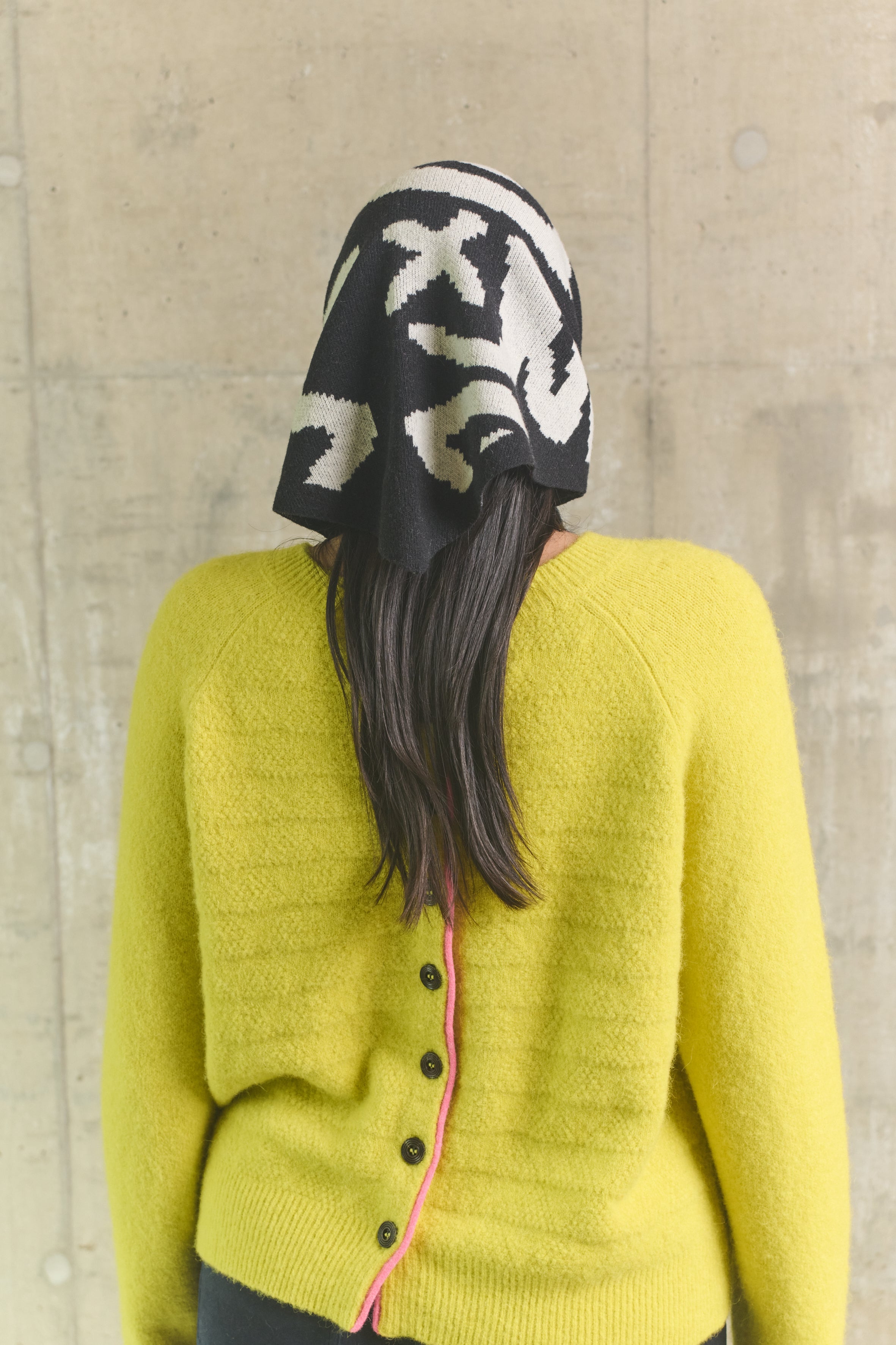 Person wearing a yellow cardigan and black and white patterned hat against a plain background