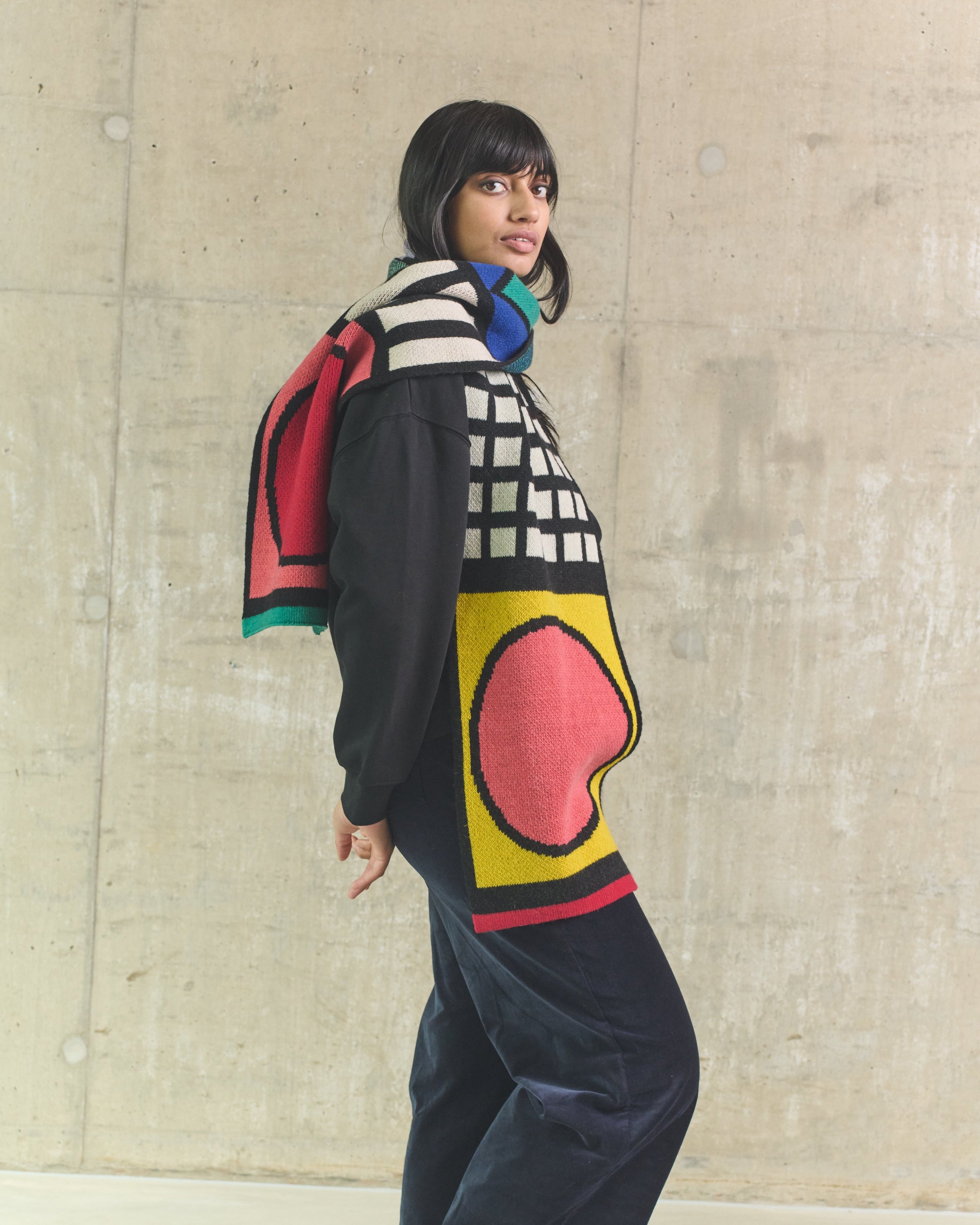 Person wearing a colorful sweater with abstract patterns against a concrete wall.