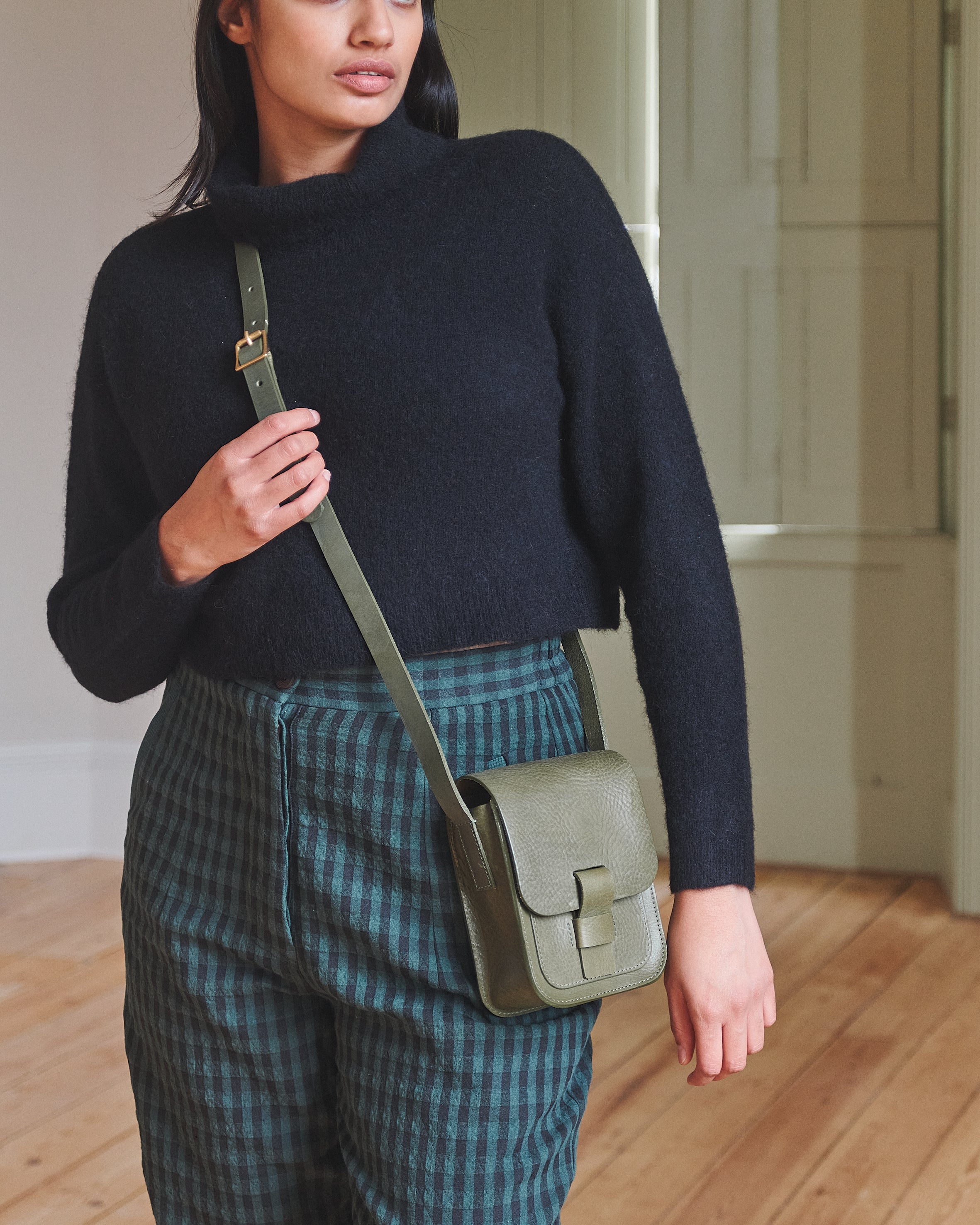 Woman holding a green crossbody bag in an indoor setting