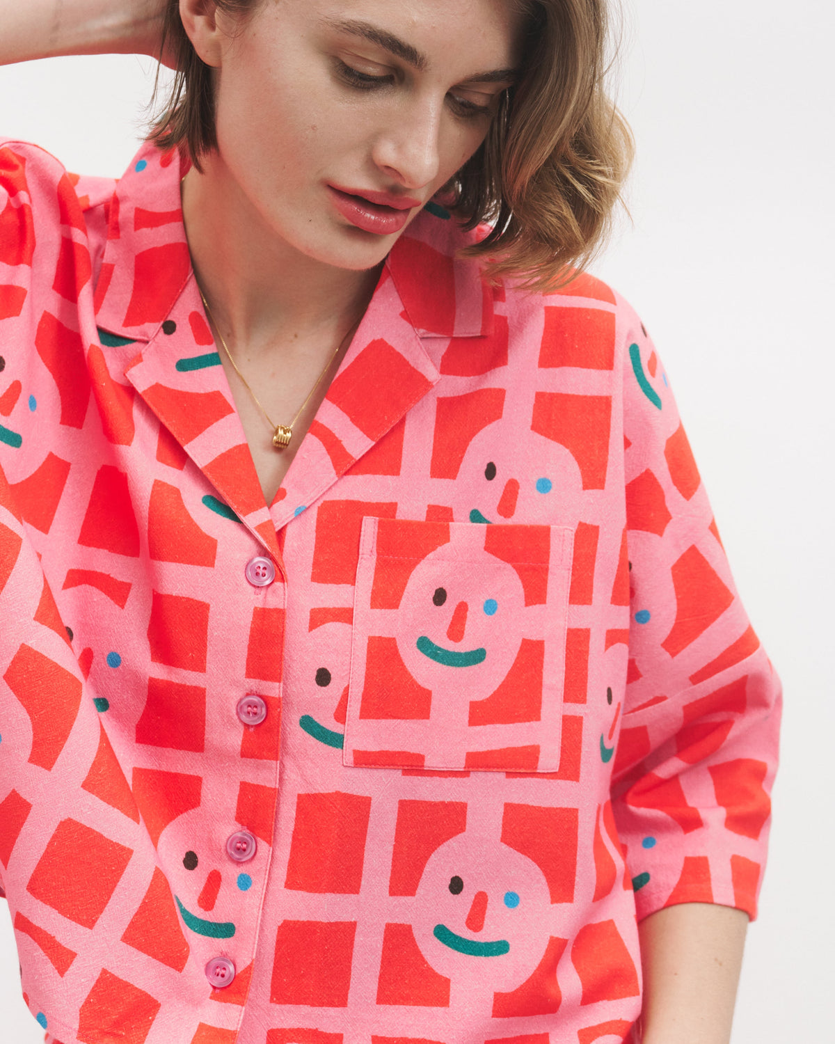 Woman wearing a red and pink patterned shirt with smiley face designs on a white background