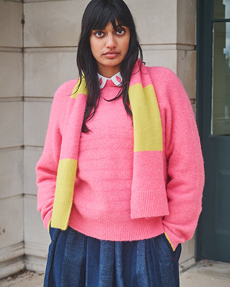 Person wearing a pink sweater with a yellow scarf in an urban setting