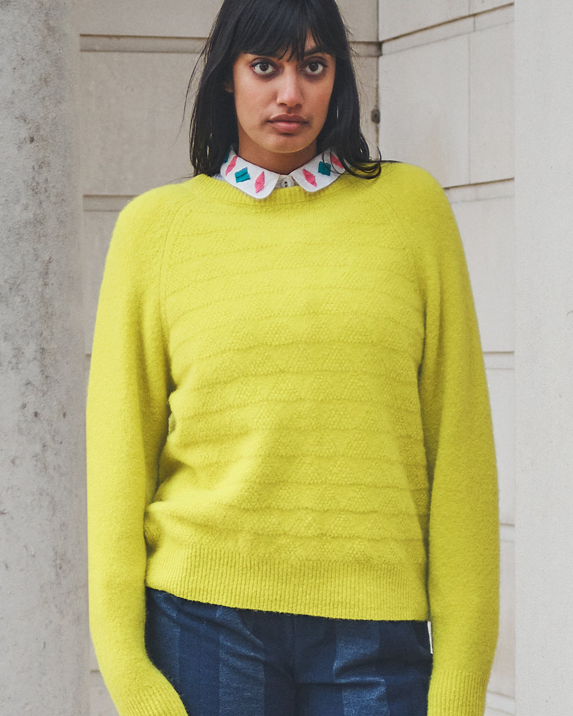 Woman wearing a bright yellow sweater with a patterned collar against a neutral wall.