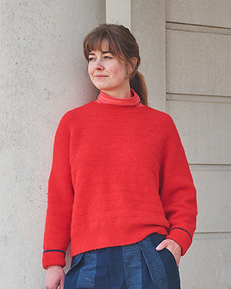Woman wearing a red sweater standing against a light-colored wall.