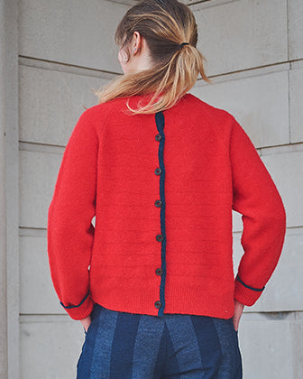 Person wearing a red cardigan with black buttons against a light gray wall.