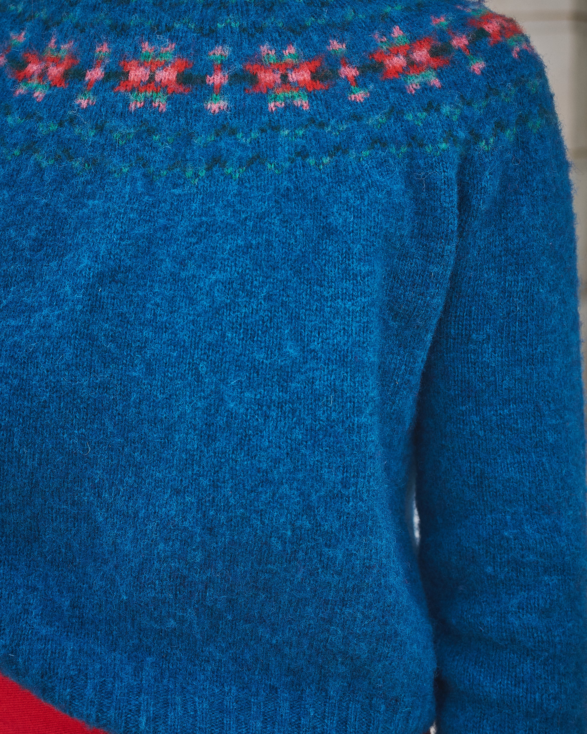 Blue knitted sweater with floral patterns on the shoulders against a neutral background