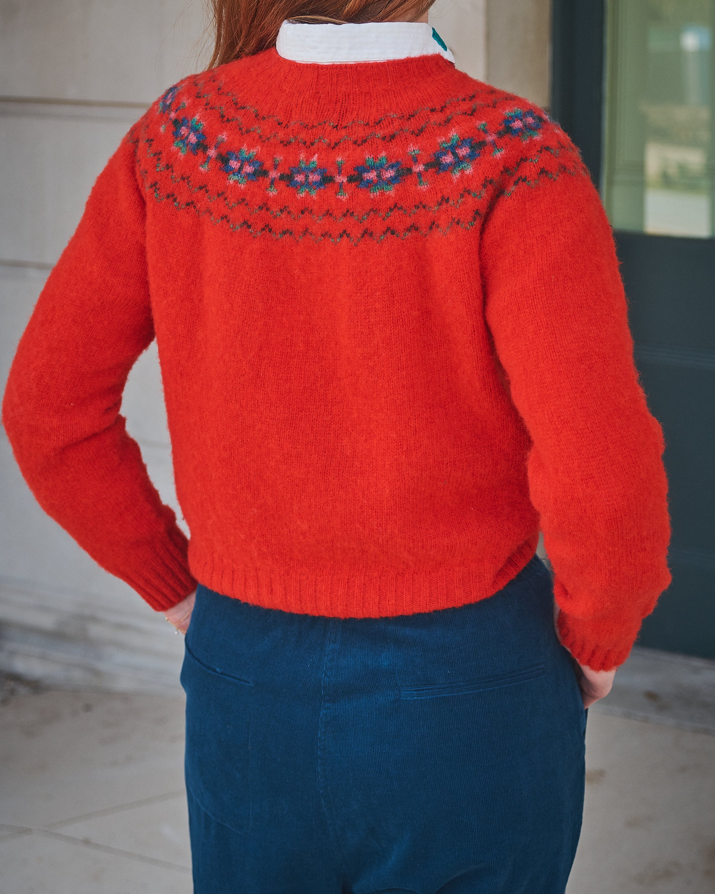 Person wearing a red sweater with a patterned yoke, standing against a neutral background.