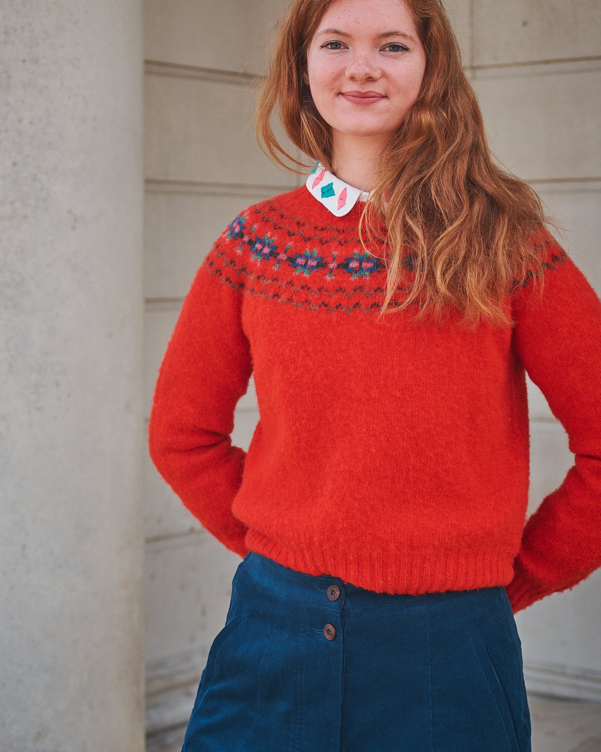 Person wearing a red sweater with a pattern, standing against a light-colored wall.