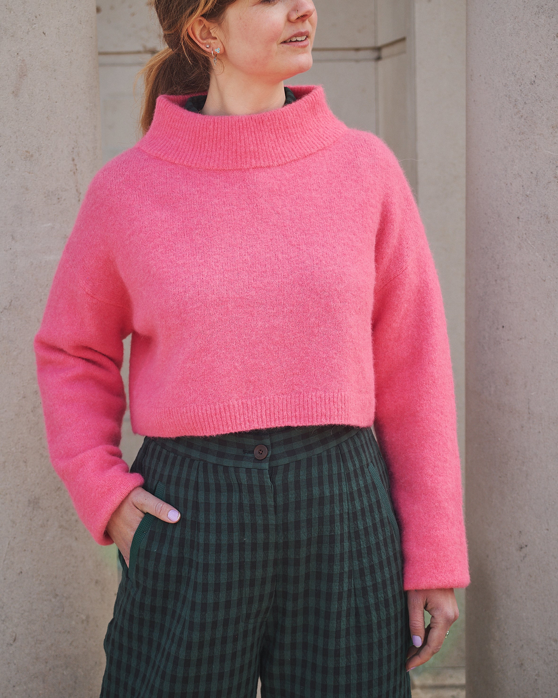 Person wearing a bright pink sweater and dark plaid pants against a neutral background