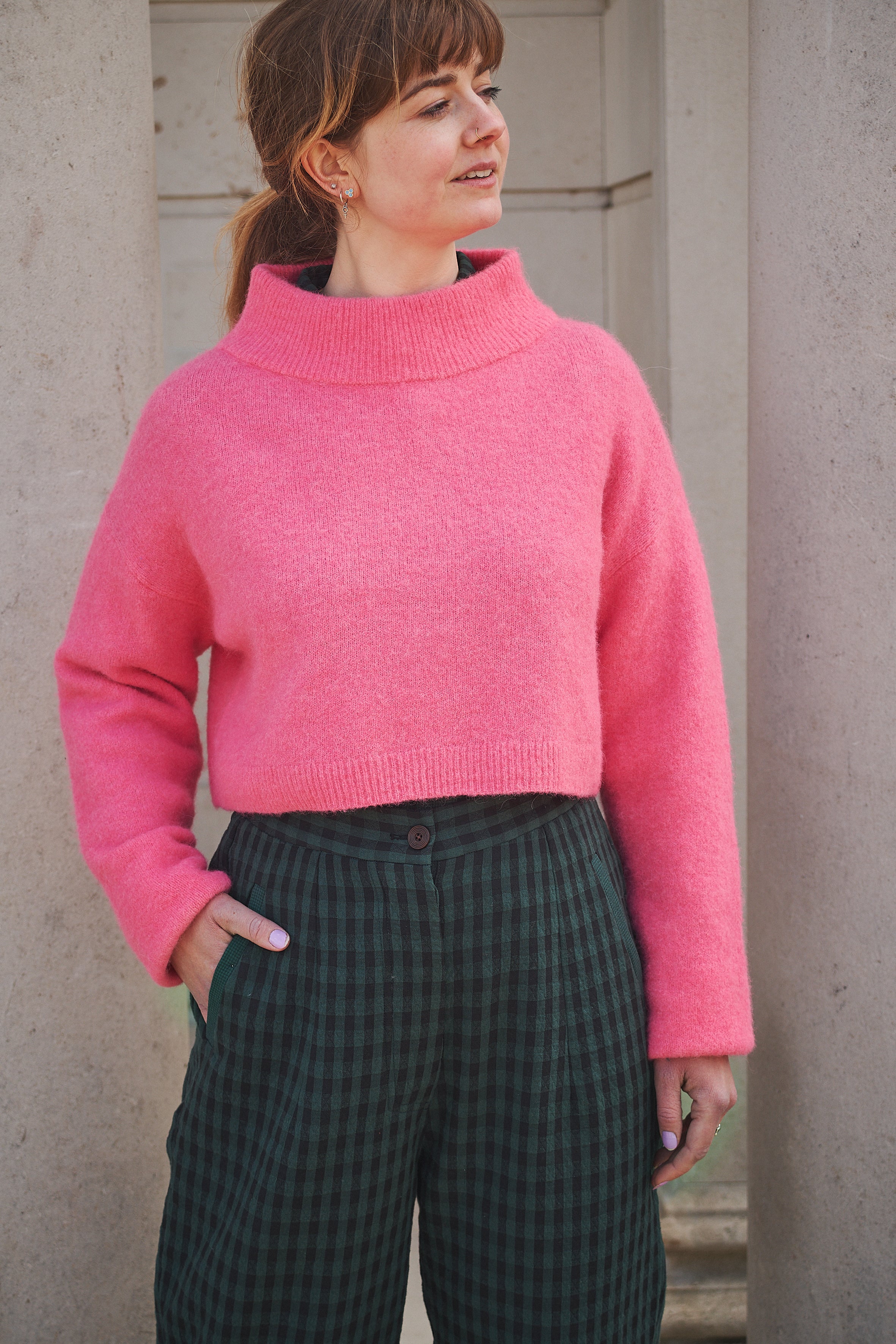Person wearing a bright pink sweater and dark plaid pants against a neutral background