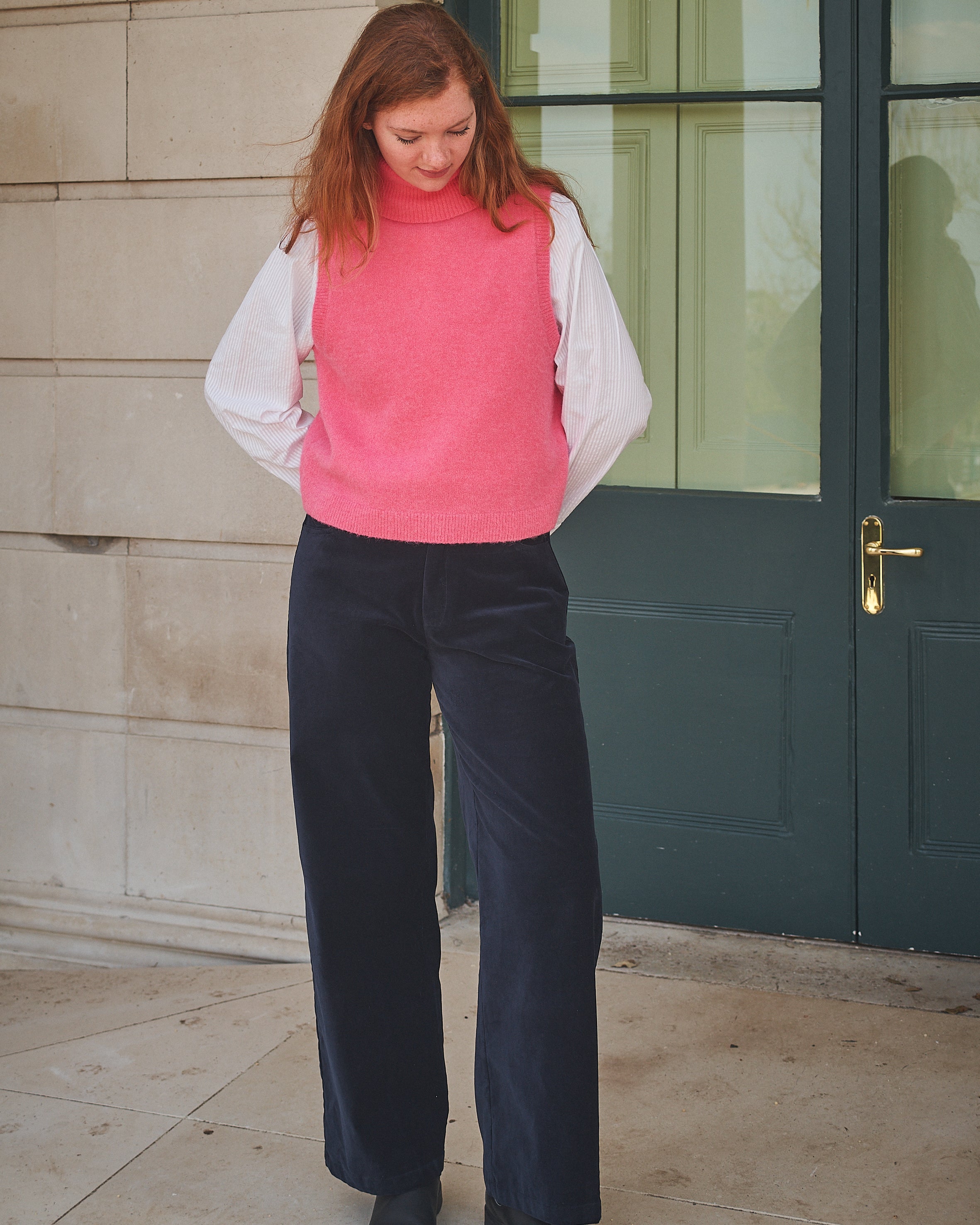 Person wearing navy pants and a red top standing against a stone wall.