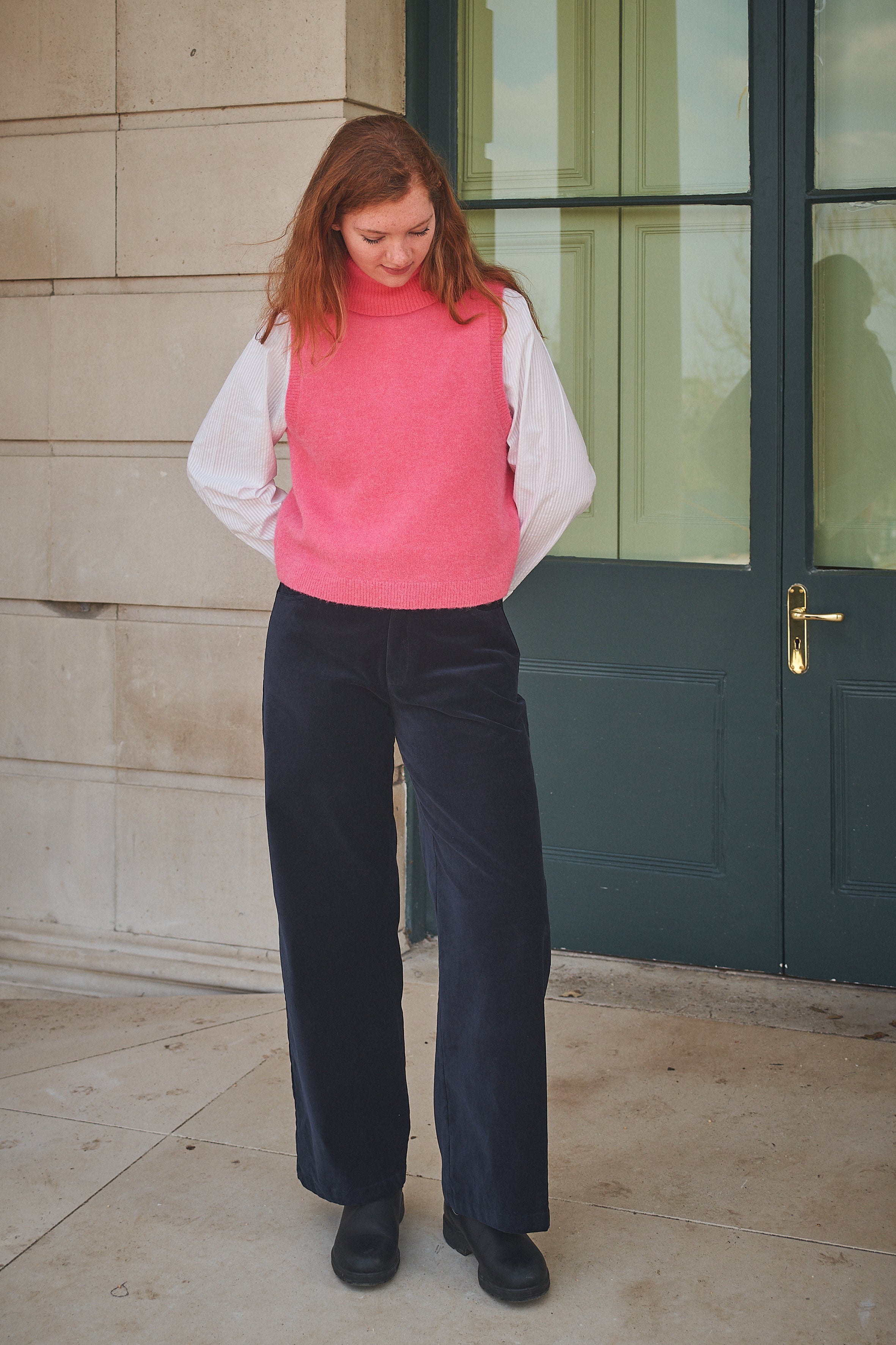 Person wearing navy pants and a red top standing against a stone wall.