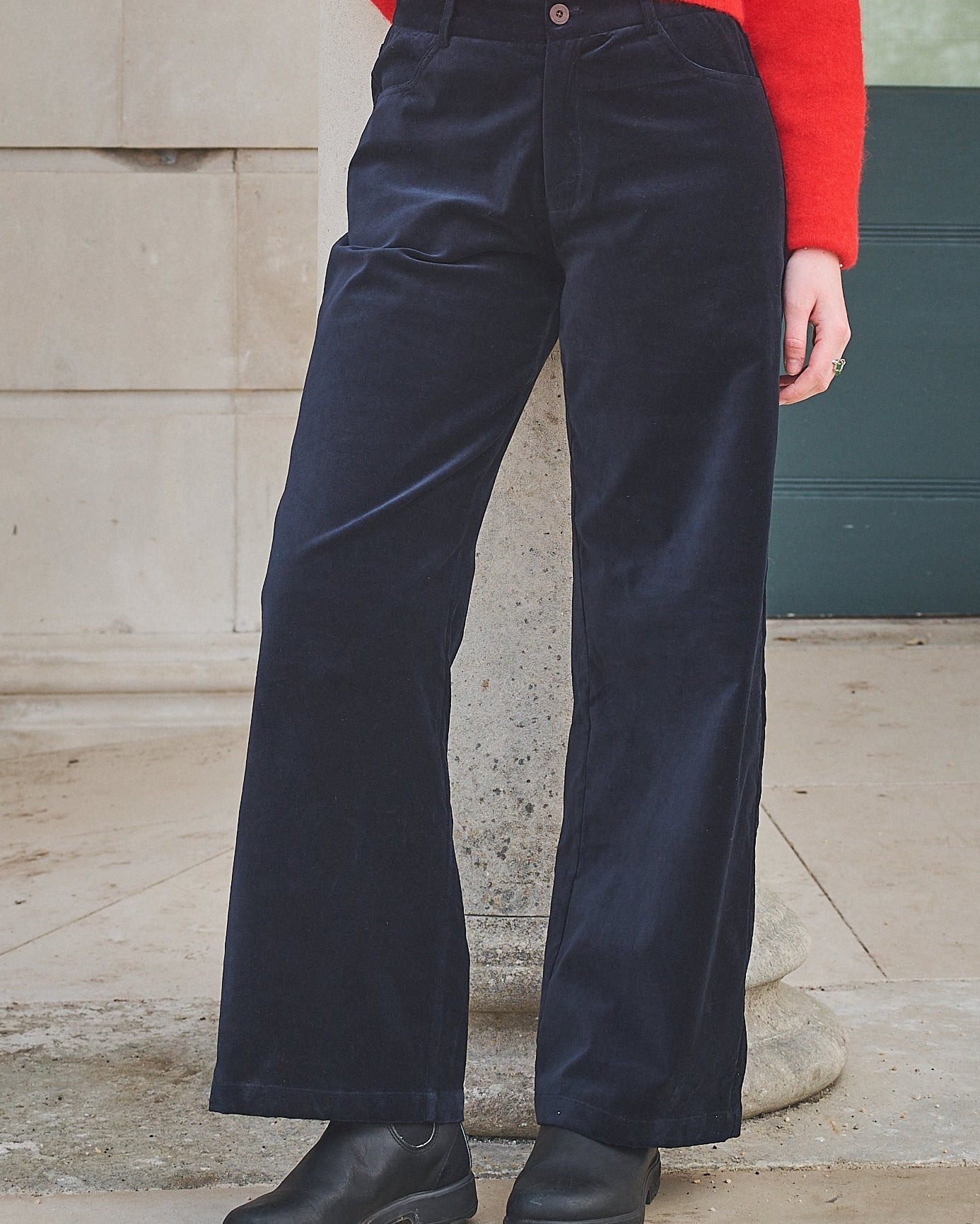 Person wearing navy pants and a red top standing against a stone wall.