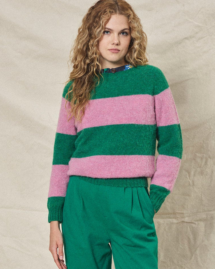 Woman wearing a green and pink striped sweater with green pants against a beige background