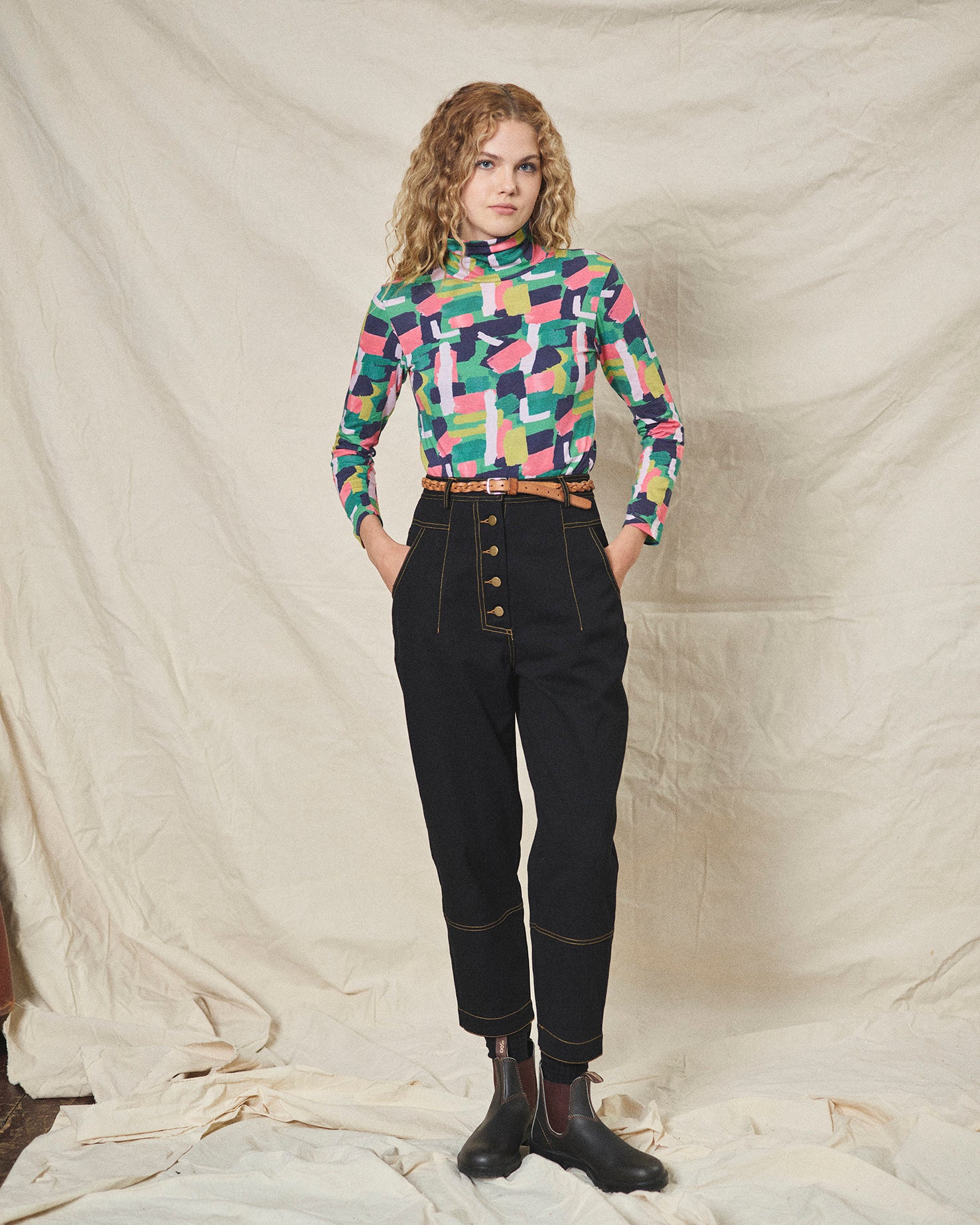 A pair of black cotton drill trousers with a high waist, wide beltband, and 5 button fly front. Features include slanted side pockets and raw stitching.